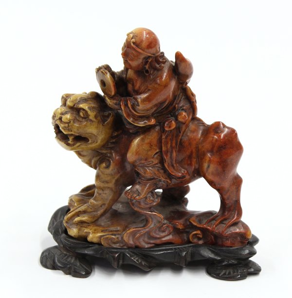 Chinese Soapstone Carving, Immortal on Tiger: Chinese soapstone figural carving, sculpted with a male figure carrying a double gourd vessel on his back and peaches suspended from his sides while holding a bi-disk and surmounted on a muscular beas