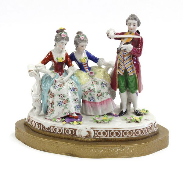Porcelain centerpiece: Porcelain centerpiece depicting two ladies sitting on a bench and a gentleman playing the violin, all dressed in classic attire in a rural environment, mounted on an oval shaped patinated metal base w