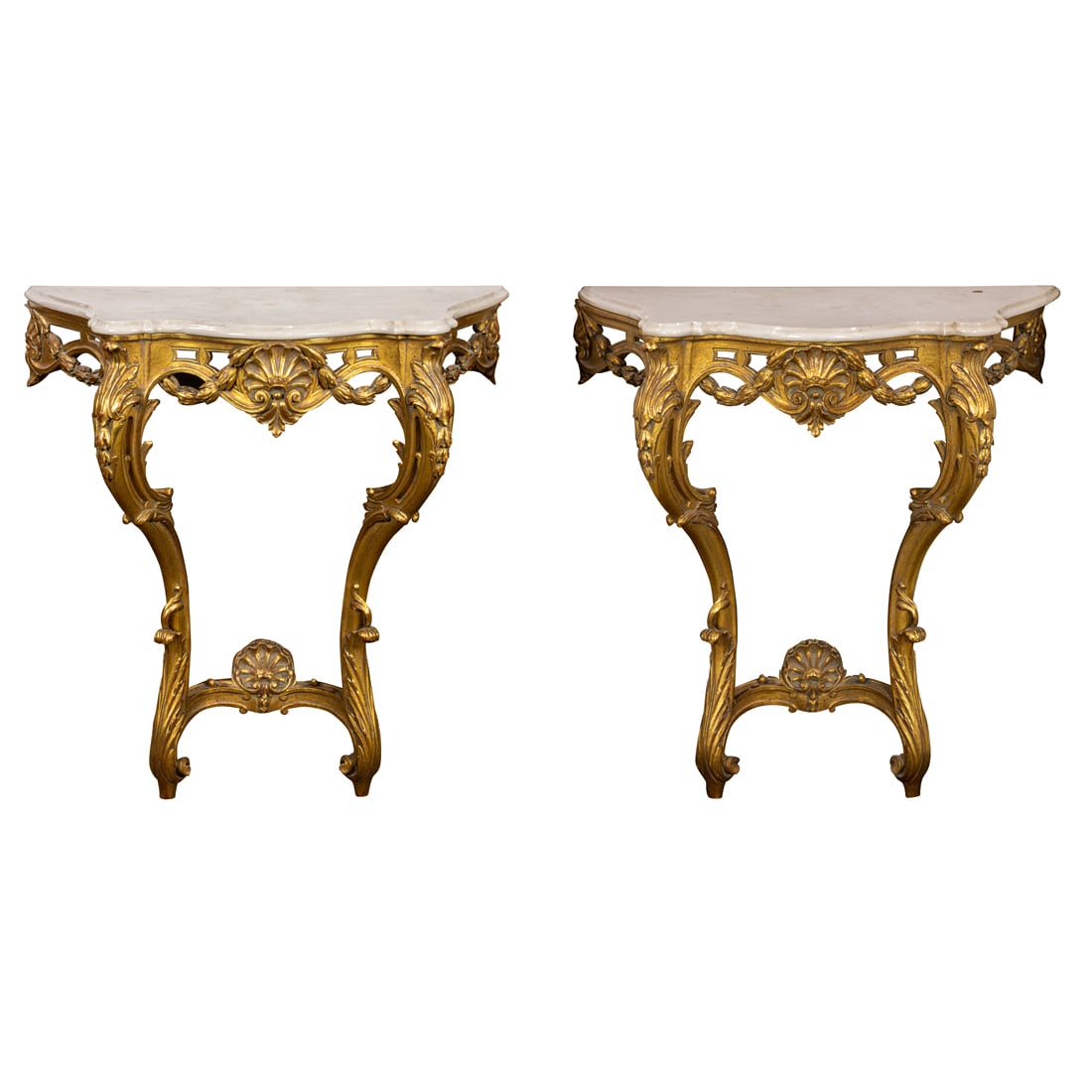 A pair of Rococo style giltwood console tables: A pair of Rococo style giltwood console tables, each with a marble top resting on the pierced serpentine apron centered with a shell and garland decorated medallion, and rising on inswept legs, 35.5"h