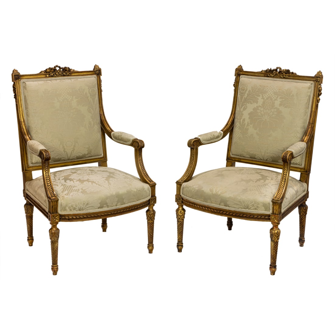 A pair of Louis XVI giltwood carved fauteuils circa 1860: A pair of Louis XVI giltwood carved fauteuils circa 1860, the well carved ribbon and floral carved crest above the damask covered upholstery, the frame with extensive detail and rising on acanthus and