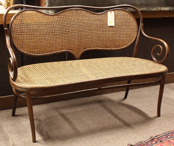 Thonet bentwood settee: Thonet bentwood settee, the shaped back centered with a serpentine reserve having a cane foundation centering the two swans neck arms terminating at the seat and rising on turned legs, retains Thonet 