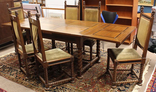 Baroque style dining suite: (lot of 10) Baroque style carved oak dining suite, c. 1930, the dining table with ebonized panels continuing to the draw leaves and rising on turned legs ending on bun feet 30''h x 94''w (extended) x