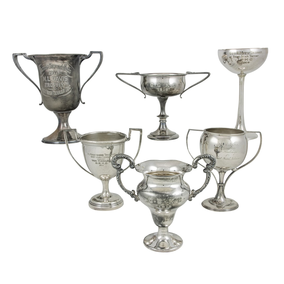 A collection of Art Nouveau and Art Deco Dog Show mostly silverplate trophy cups or urns, comprising: A collection of Art Nouveau and Art Deco Dog Show silver trophy cups or urns, comprising a Shreve & Co. sterling cup 'Geo. H. Pippy Trophy Best Irish Terrier P.K.C. 1914' en suite with five plated exa