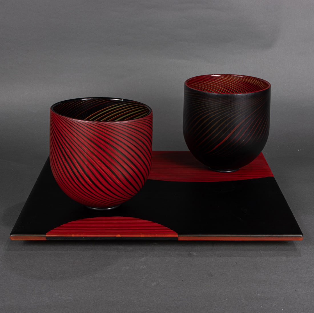 A Steven Klein glass bowl and tray sculpture: Balance 64: A Steven Klein glass bowl and tray sculpture: Balance 64, 2007, glass, composed of two red and black stripe bowls on a square plinth, vessels greatest: 7"h x 7"dia; base: 1.25"h x 18.5"w. Provenance: