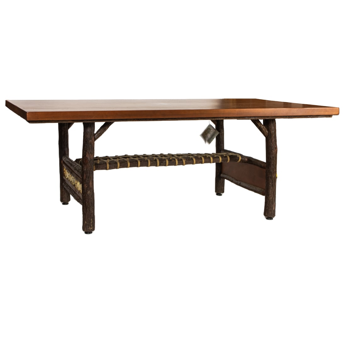 An Old Hickory walnut dining table, fashioned in the rustic style, the slab form top rising on: An Old Hickory walnut dining table, fashioned in the rustic style, the slab form top rising on sapling branch form trestle supports with a center woven leather shelf, 31"h x 84"w x 42"d. Note: Portion