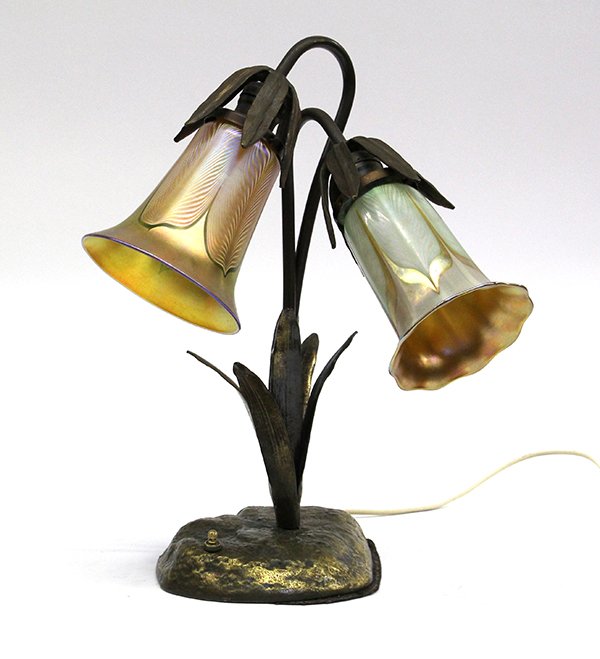 Arts and Crafts patinated metal table lamp: Arts and Crafts patinated metal table lamp, early 20th century, the two light fixture of lily form terminating at the signed Quezal pulled feather shades, and rising on a naturalistic base, 15''h x 13