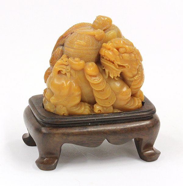 Chinese Stone Carving, Qilin: Chinese carved soapstone figural group, featuring a qilin supporting a covered basket on its back, along with a monk reading an open book on top of the box, further accented with ingots and cash coins