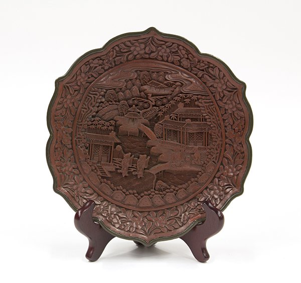 Chinese Cinnabar Plate: Chinese carved cinnabar lacquered plate, of foliate form centered with a scene of scholars outside of villa complexes, in contrast with the sides decorated with flowering sprigs, with an apocryphal Qi