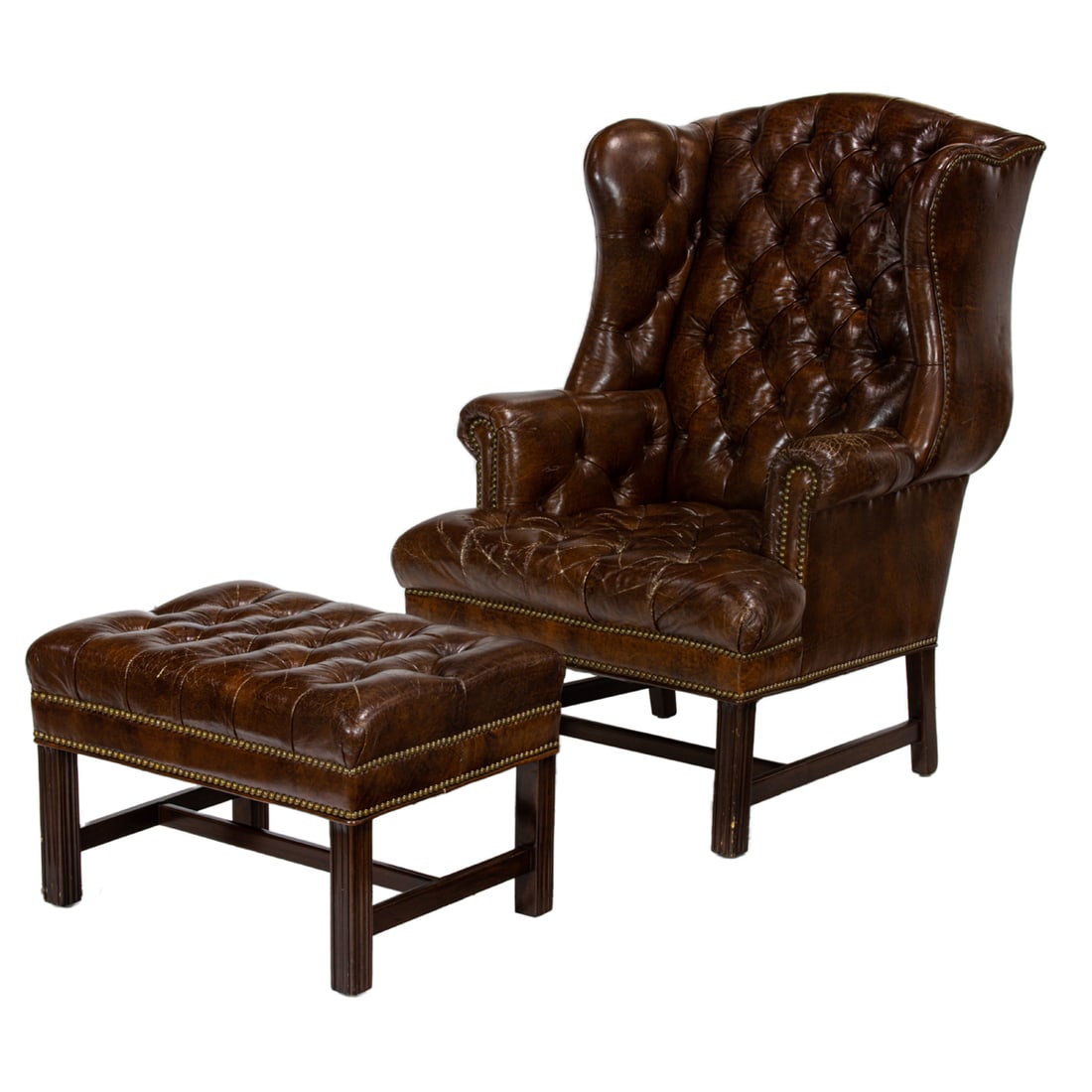 A Victorian style tufted and upholstered armchair and ottoman: A Victorian style tufted and upholstered armchair and ottoman, of wing back form, upholstered in brown vegan leather and finished with brass nailhead trim, rising on fluted block legs, 44.5"h x 29"w x