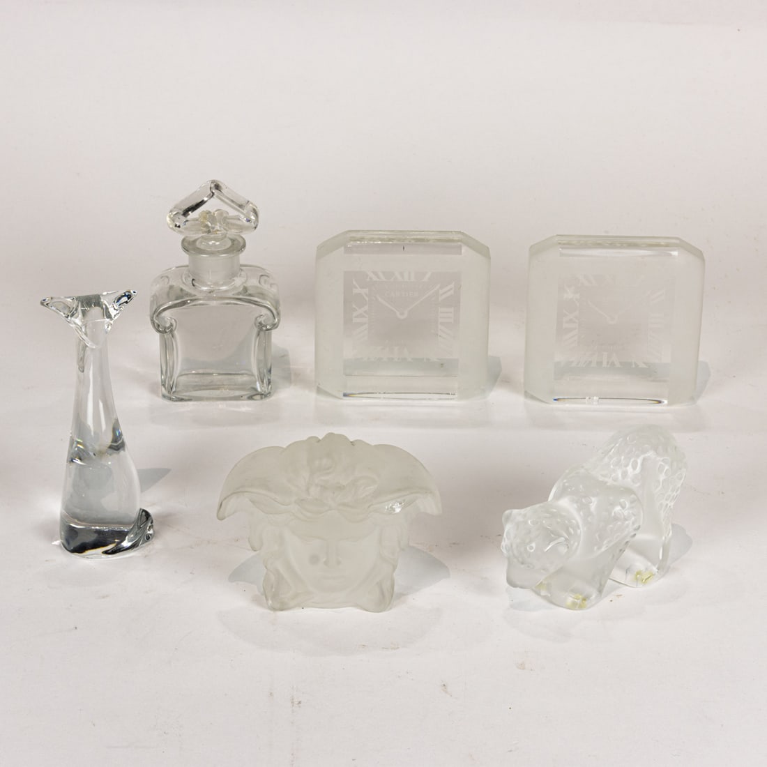 An assembeled group of glass including Lalique, Cartier, Baccarat and Versace: An assembeled group of glass, comprising (1) Lalique leopard cub (1) Rosenthal for Versace head; (2) Cartier 'clock' paperweights; Baccarat for Guerlain bottle; Baccarat stylized seated cat, greatest