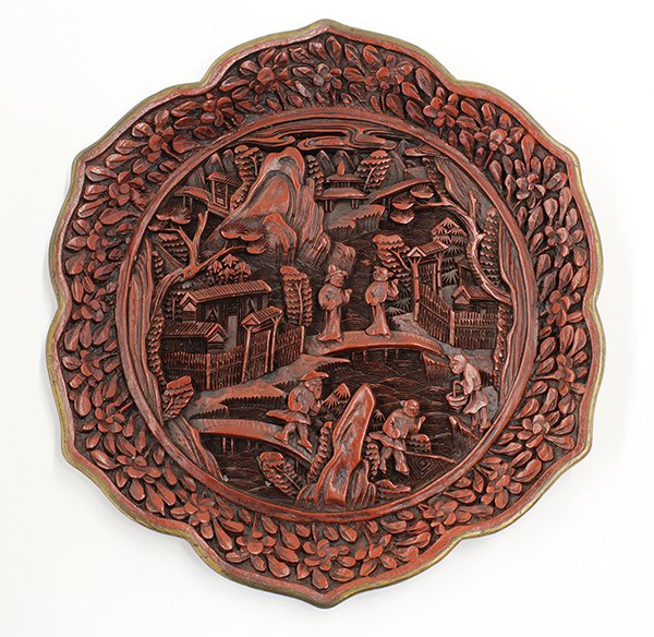 Chinese Cinnabar Lacquered Dish: Chinese cinnabar lacquered foliate dish, the well featuring a scenic rustic village with figures crossing the bridge, encircled by the side decorated with flowering sprigs, the base with an apocrphyal