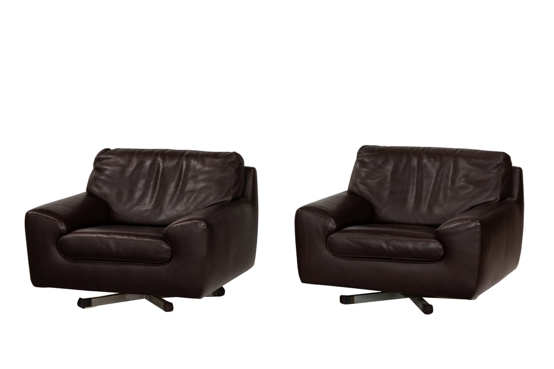 A pair of Roche Bobois brown leather overstuffed club chairs: A pair of Roche Bobois brown leather overstuffed club chairs, the wide form fitted with loose seat cushions and raised on swivel base, 28"h x 37"w x 32" seat height 16"