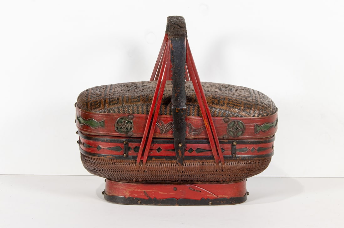 A Chinese oval shaped basket with lid and handle: A Chinese oval shaped basket with lid and handle. The woven cane and bamboo basket decorated on lid with Chinese characters, rising on a bamboo. 15" high.