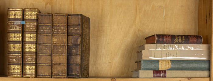 Two shelves of antique leather or cloth books together with oversized modern art books