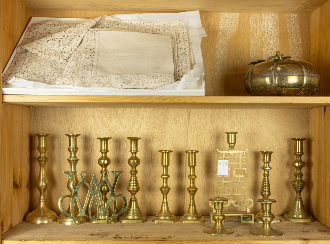 An assembled group of brass tableware and linens: An assembled group, comprising (4) pair of brass candlesticks; (3) single candlestick; (1) Williamsburg monogram brass trivet; Chinese brass gourd form box and a boxed set of linen and lace placemats