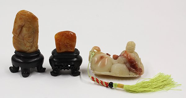 Three Chinese Soapstone Carvings: (lot of 3) Chinese soapstone small carvings, consisting of a caramel colored pebble carved with a man crouched below a tree; the second of a honey hue with figures crossing a bridge reversed by schola