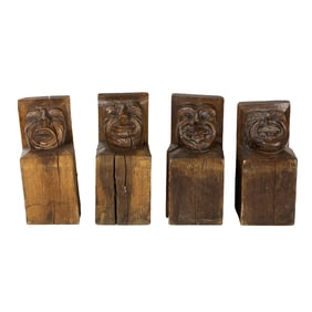 A set of four carved wood corbels or architectural rafter tails with grotesque grinning faces