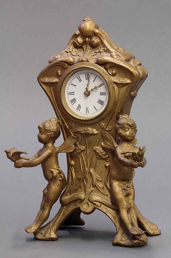 Louis Pierlot gilt metal dresser clock: Louis Pierlot gilt metal dresser clock, the floral decorated crest rising above the Roman numeral dial flanked by two fairies holding doves, and rising on four feet, 9"h