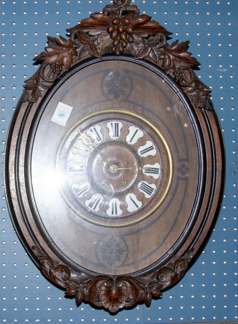 An oak wall clock, the dial having enamel roman numerals: An oak wall clock, the dial having enamel roman numerals, in case surmounted by carved grape ivy carvings in high relief, 26"h x 18.75"w