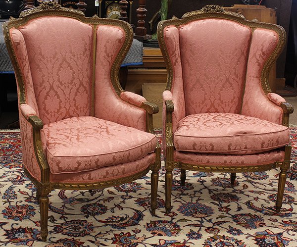 Pair of giltwood carved bergeres: Pair of giltwood carved bergeres, early 2oth century, the wing back form surmounted with a floral carved crest centering the acanthus carved body continuing to the padded arms, the shaped returns with