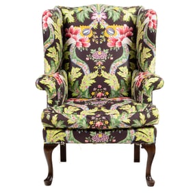 A wing chair upholstered in green, pink and blue floral pattern on brown ground