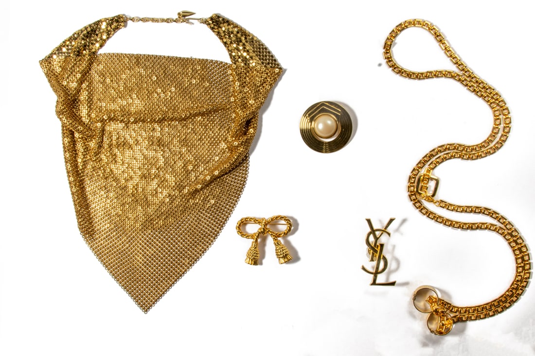 Five pieces of costume jewelry comprising Trifari, Whiting and others: Five pieces of gold tone costume jewelry comprising (1) Trifari necklace; (1) Whiting gold mesh necklace; (3) gold tone brooches, including a YSL-logo example. [5 total}