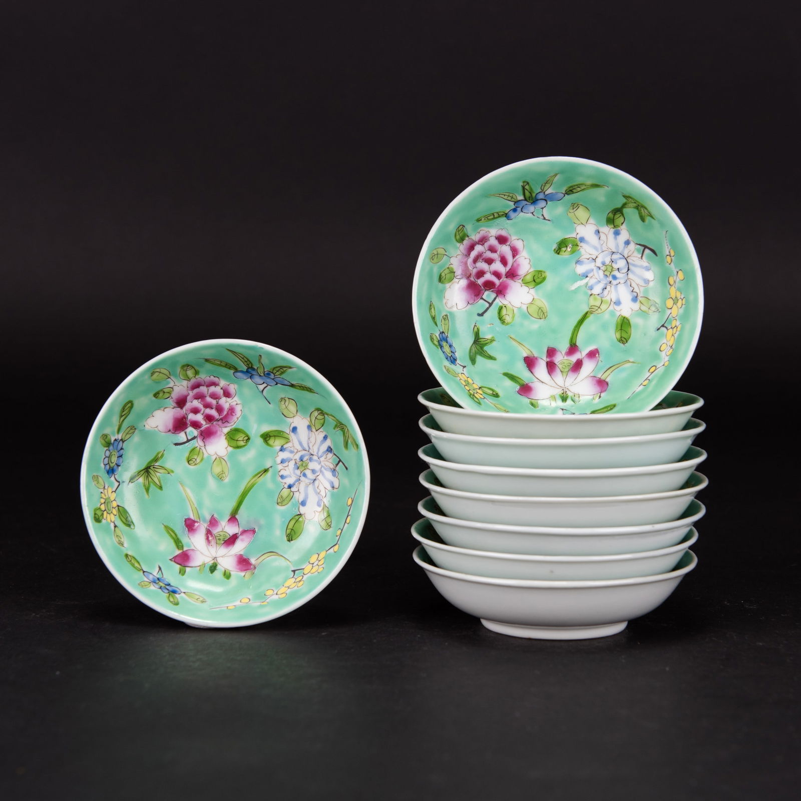 A Group of 9 Famille Rose Saucer Dishes: (lot of 9) A group of famille rose saucer dishes, each of shallow rounded form, decorated with flower blossoms of peony, chrysanthemum and lotus, all reserved on a turquoise ground. 0.98"h x 3.94"d (2