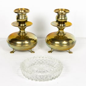 A pair of Dutch brass candlesticks, each raised on tripod supports, together with a glass ashtray