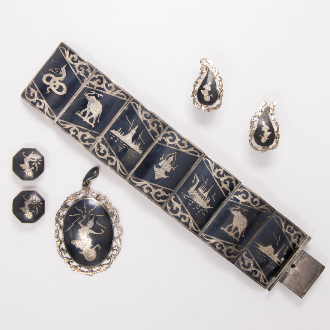 A Thai sterling silver jewelry set: A Thai sterling silver jewelry set Comprising a bracelet, pendant, and two pairs of ear clips designed with Thai figural motifs; gross weight: 80.25 grams