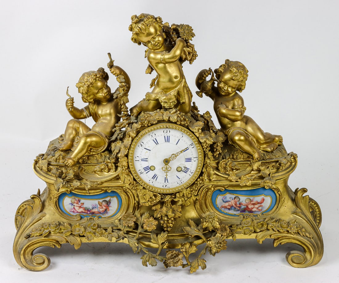A Louis XV style gilt bronze and Sevres style clock case: A Louis XV style gilt bronze and Sevres style porcelain mounted clock case, 19th century, modeled as three Bacchanalian putti raised on a plinth inset with clock dial and scrolled foliate decorated pl