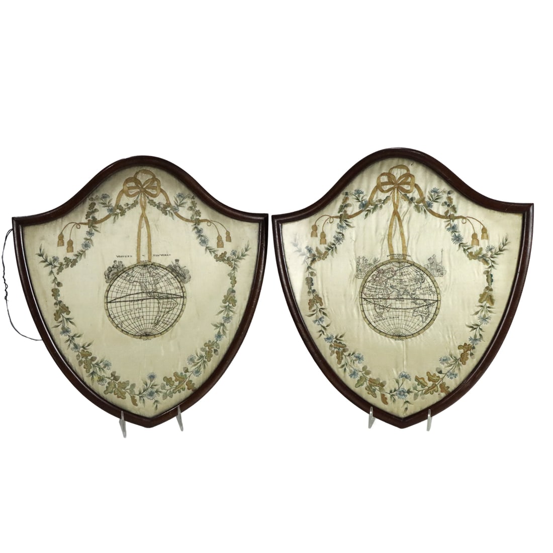 A pair of Regency silk embroidered map pictures: A pair of Regency silk embroidered map pictures, early 19th century, each depicting the Eastern and Western Hemispheres worked in silk threads within a ribbon-tied floral garland border, housed in
