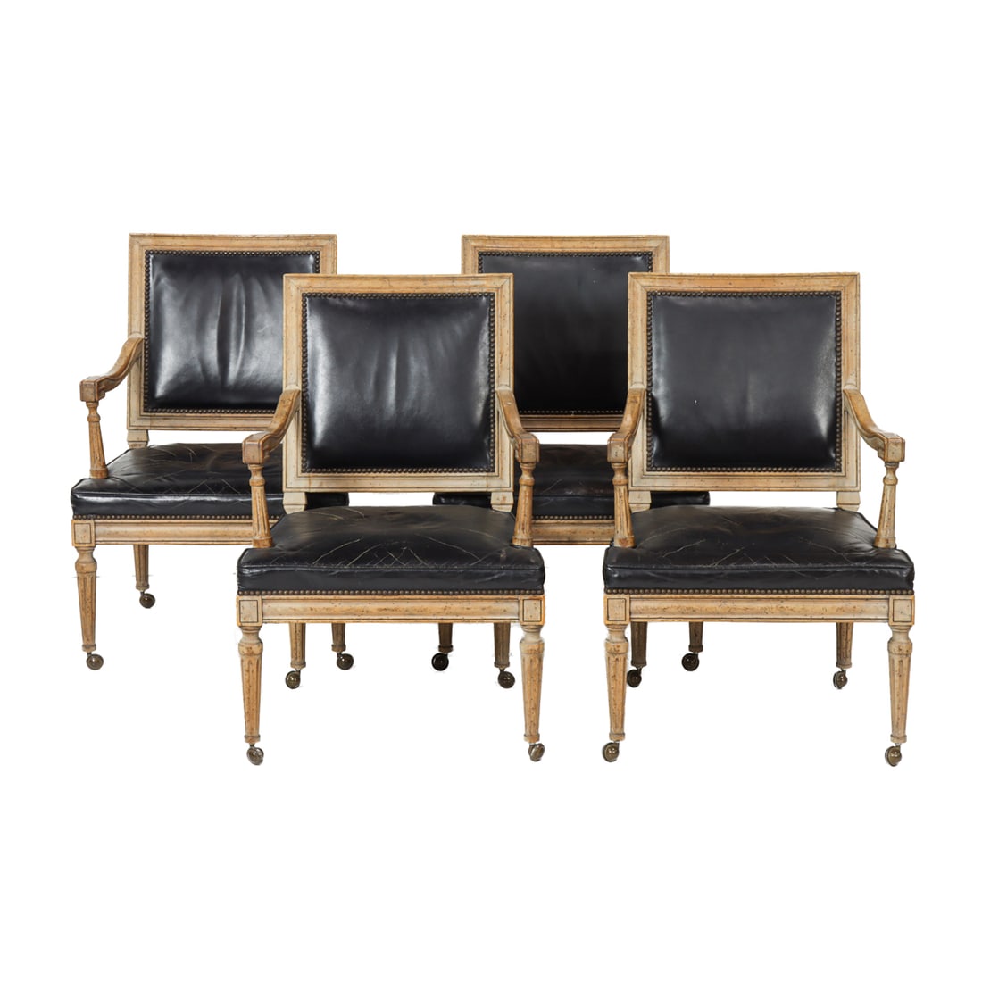 A set of four armchairs in the Neoclassical taste circa 1890: A set of four armchairs in the Neoclassical taste circa 1890, each with black leather upholstered seat and back with nail head trim, and rising on fluted legs, 33"h x 23"w x 19"d