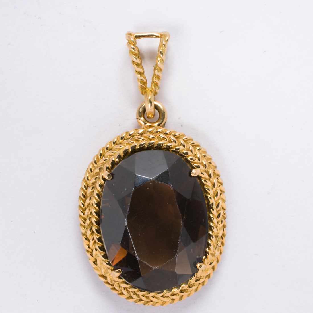 A smokey quartz and 18k gold pendant: A smokey quartz and 18k gold pendantCentering an oval-cut smokey quartz measuring approximately 20.26 x 15.25 x 8.75 mm, framed within 18k gold bezel designed as twisted rope; length: 1 5/8 in; 10.00