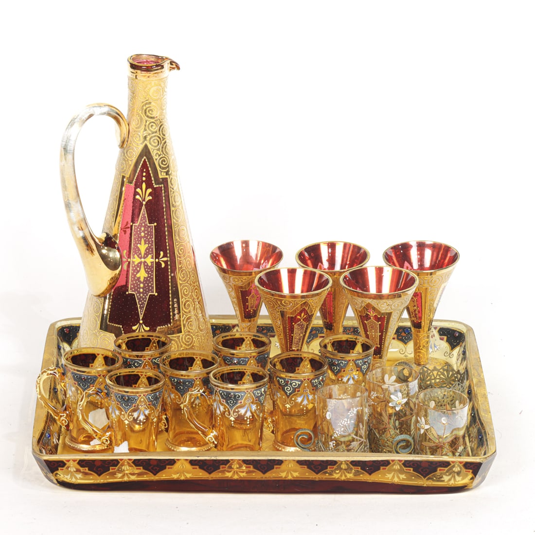 A group of Continental enamel and gilt decorated liqueur sets: A group of Continental enamel and gilt decorated liqueur sets, including (1) Bohemian in the Moser style amber glass tray and (8) matching handled cups; (3) cups in metal filigree frames; (1)