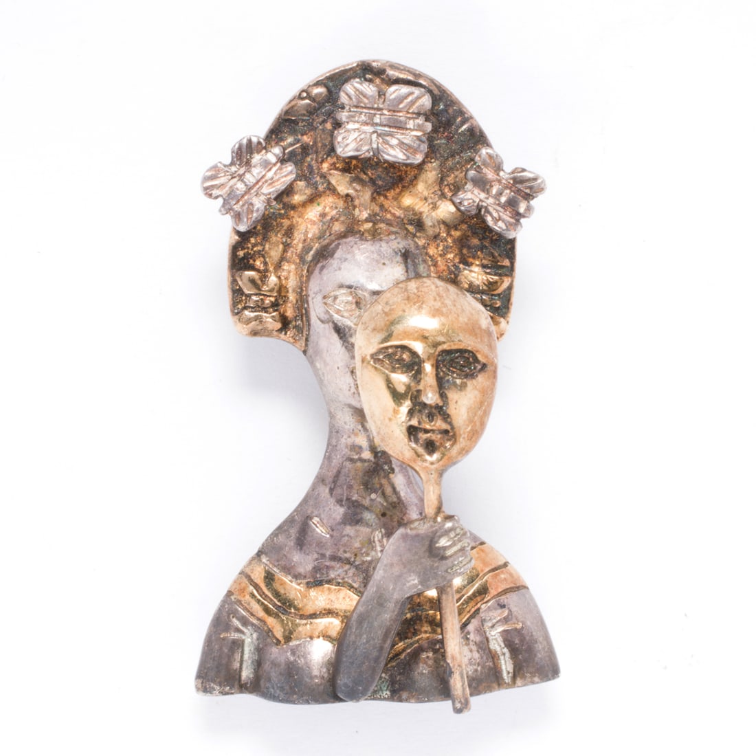A Sergio Bustamante silver and gold Madame Butterfly brooch: A Sergio Bustamante silver and gold Madame Butterfly broochDesigned as a sterling silver woman holding a mask, accented by gold and surrounded by a halo of butterflies; length: 1 3/4 in; 21.10 grams