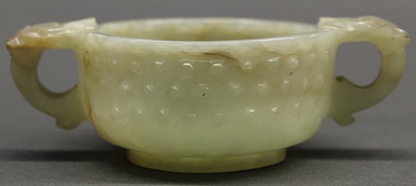Chinese Jade Libation Cup: Chinese carved jade libation cup, the body with raised bosses within a diaper pattern, all flanked by single-horned dragon form handles and raised on a short foot, the sea-green matrix with light incl