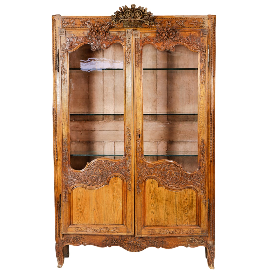A French Louis XV Provincial vitrine: A French Louis XV Provincial vitrine, 19th century, the heavily carved crest with a floral and basket crest above the two doors further decorated with floral sprays, and opening to fixed glass