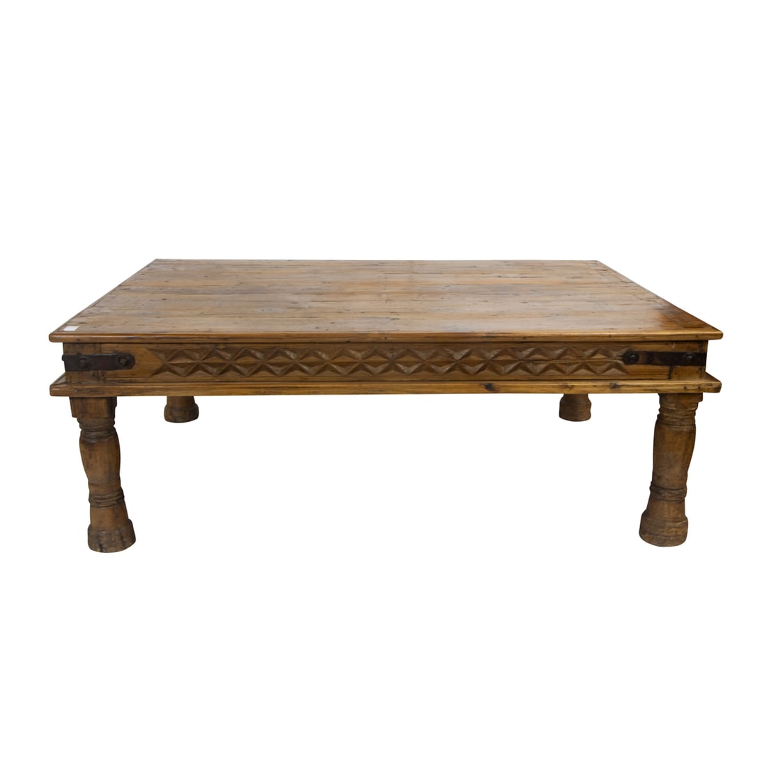 A large rustic carved cocktail table: A large rustic carved cocktail table, the plank top with a carved apron and wrought metal strap fastened corners, and rising on thick turned legs, 26"h x 71.5" x 51"d