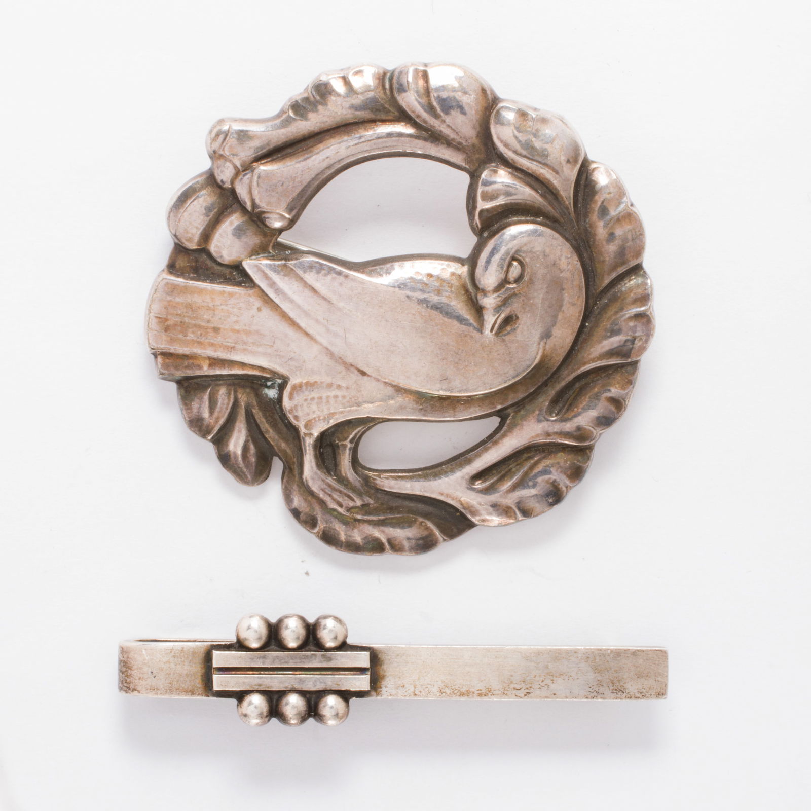 A Georg Jensen brooch and clip: A Georg Jensen brooch and clipDesign no.: 123 and 61 The brooch designed as a crow within a floriform wreath, together with a clip featuring geometric accents; brooch length: 1 3/4 in; clip length: 2