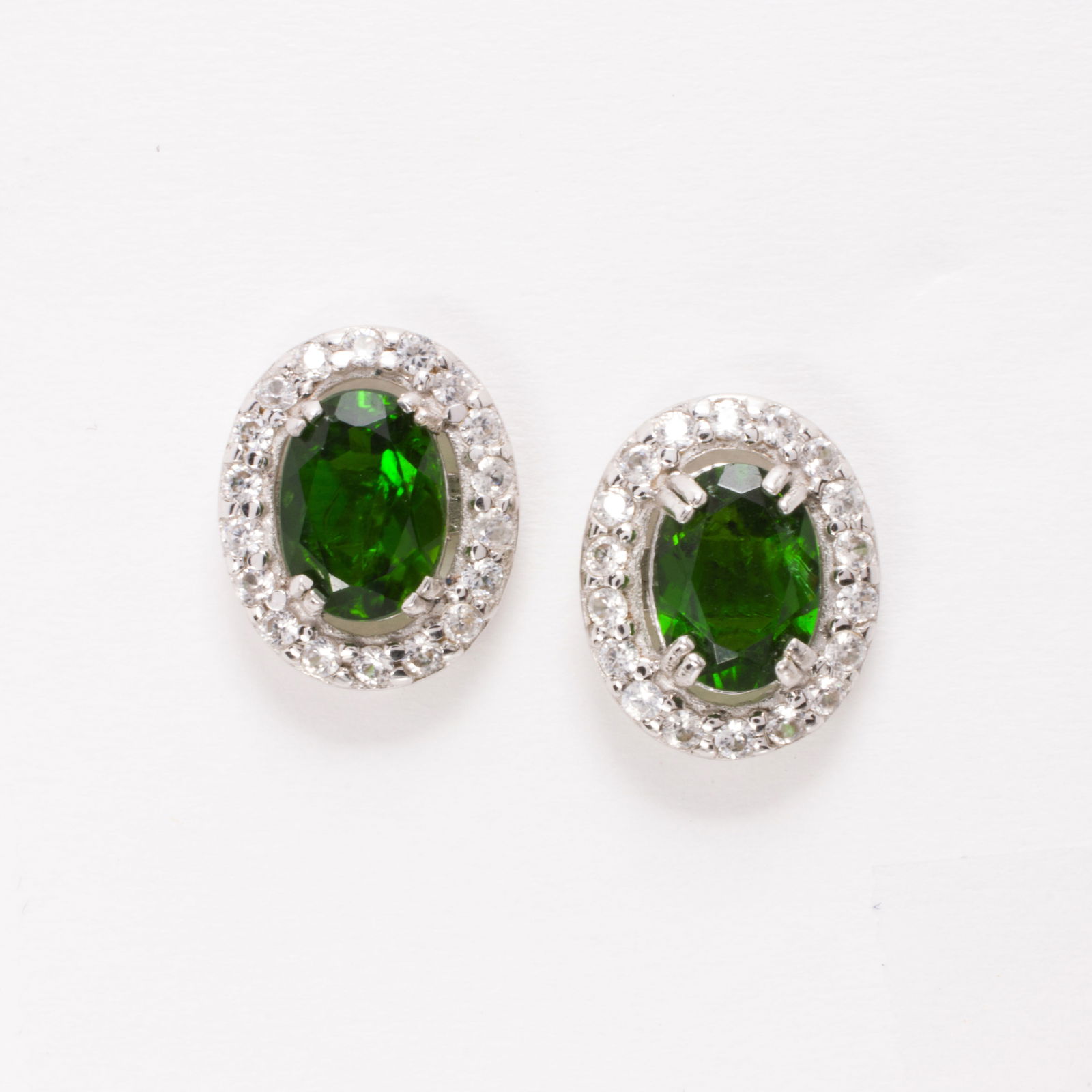 A green gemstone, zircon, and sterling silver earrings: A green gemstone, zircon, and sterling silver earringsOf stud design, centering oval-cut green gemstones weighing a total of 1.55 carats with round-cut zircon surround; 2.35 grams