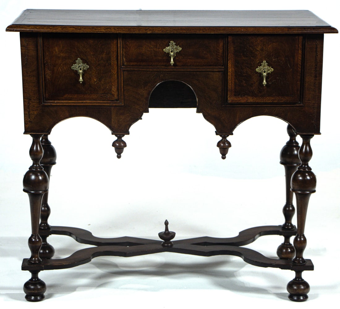 A William and Mary lowboy or dressing table: A William and Mary lowboy or dressing table, 18th century and later, the rectangular walnut top over three drawers with a scalloped apron suspending acorn finials, raised on turned legs joined by a se