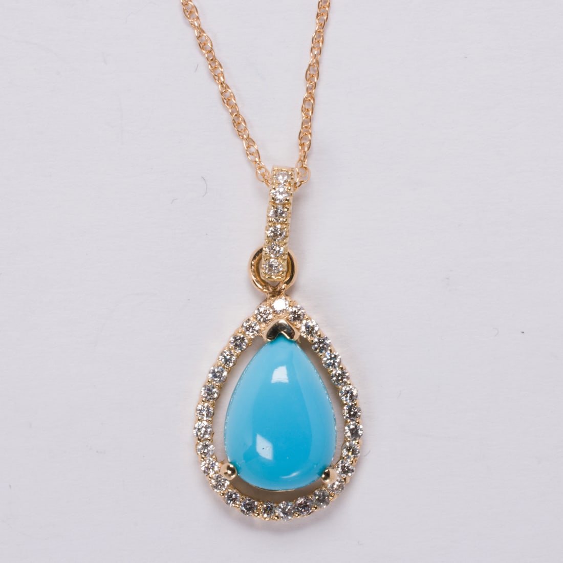 A turquoise diamond and 14k pendant necklace: A turquoise diamond and 14k pendant necklacecenteriing a pear shaped turquoise cabochon measuring 11.05 x 7.95 x 3.90 mm, framed by round brilliant-cut diamonds; pendant length: 1 in; chain length: