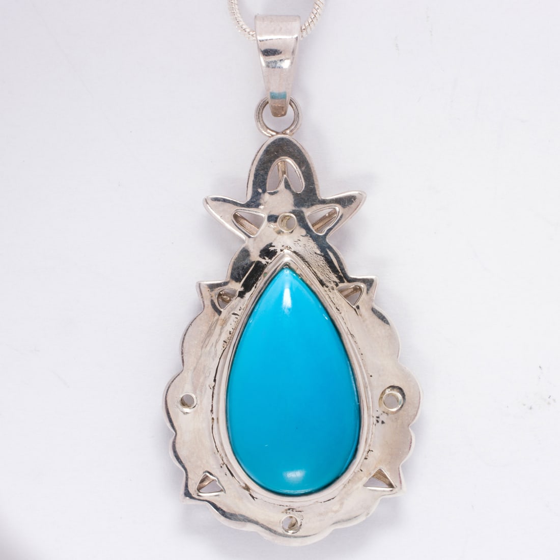 A turquoise and silver pendant: A turquoise and silver pendantCentering a pear-shaped turquoise cabochon measuring approximatley 22.13 x 12.90 mm within periced mounting on snake-link chain; chain length: 24 in; pendant length: 1