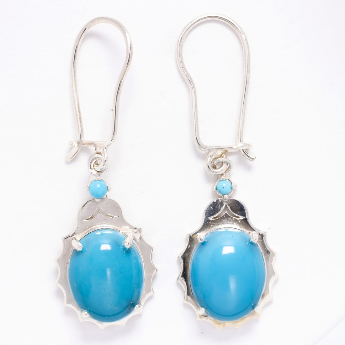 A pair of turquoise and silver earrings: A pair of turquoise and silver earringseach centering a oval shaped turquoise cabochons weighing 7.50 carats total; length: 1 1/2 in; 5.60 grams