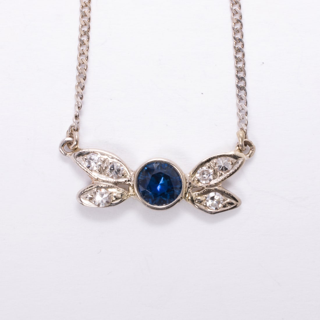 A sapphire, diamond, and 14k white gold necklace: A sapphire, diamond, and 14k white gold necklaceFeaturing a round-cut sapphire weighing 0.71 carat, framed by three single-cut diamonds on either side; length: 16 in; 3.20 grams