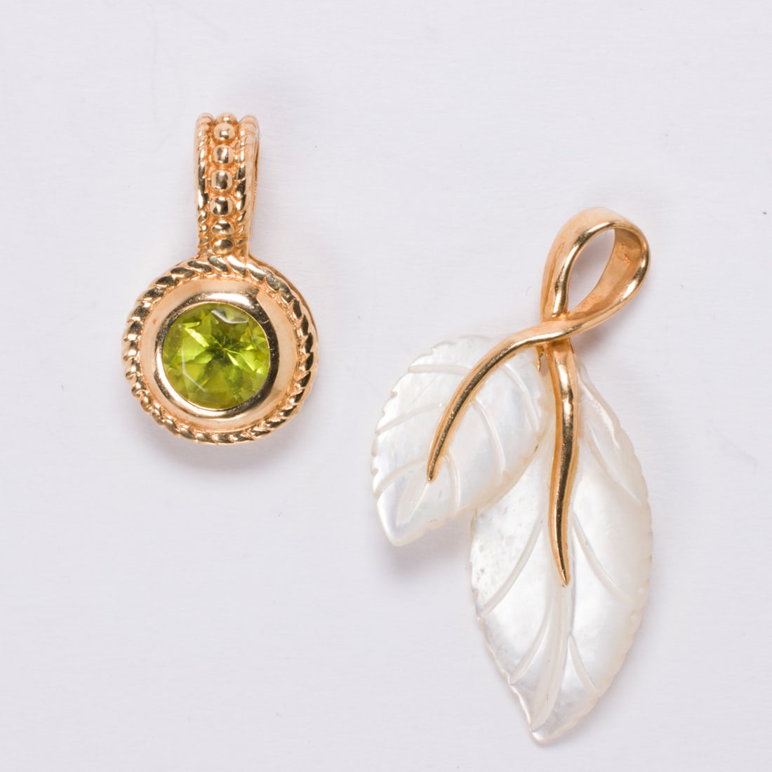Two hardstone and 14k gold pendants: Two hardstone and 14k gold pendantsComprising one mother-of-pearl and one peridot pendant, each set within 14k gold; pendant lengths: 1 1/8 in and 5/8 in, respectively; gross weight: 3.25 grams