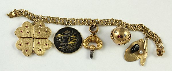 Yellow gold charm bracelet: 14K yellow gold charm bracelet set with five charms including a locket charm with 4 hearts in the shape of a four leaf clover with pink-red colored stones, one of a pocket watch key, expandable ball l