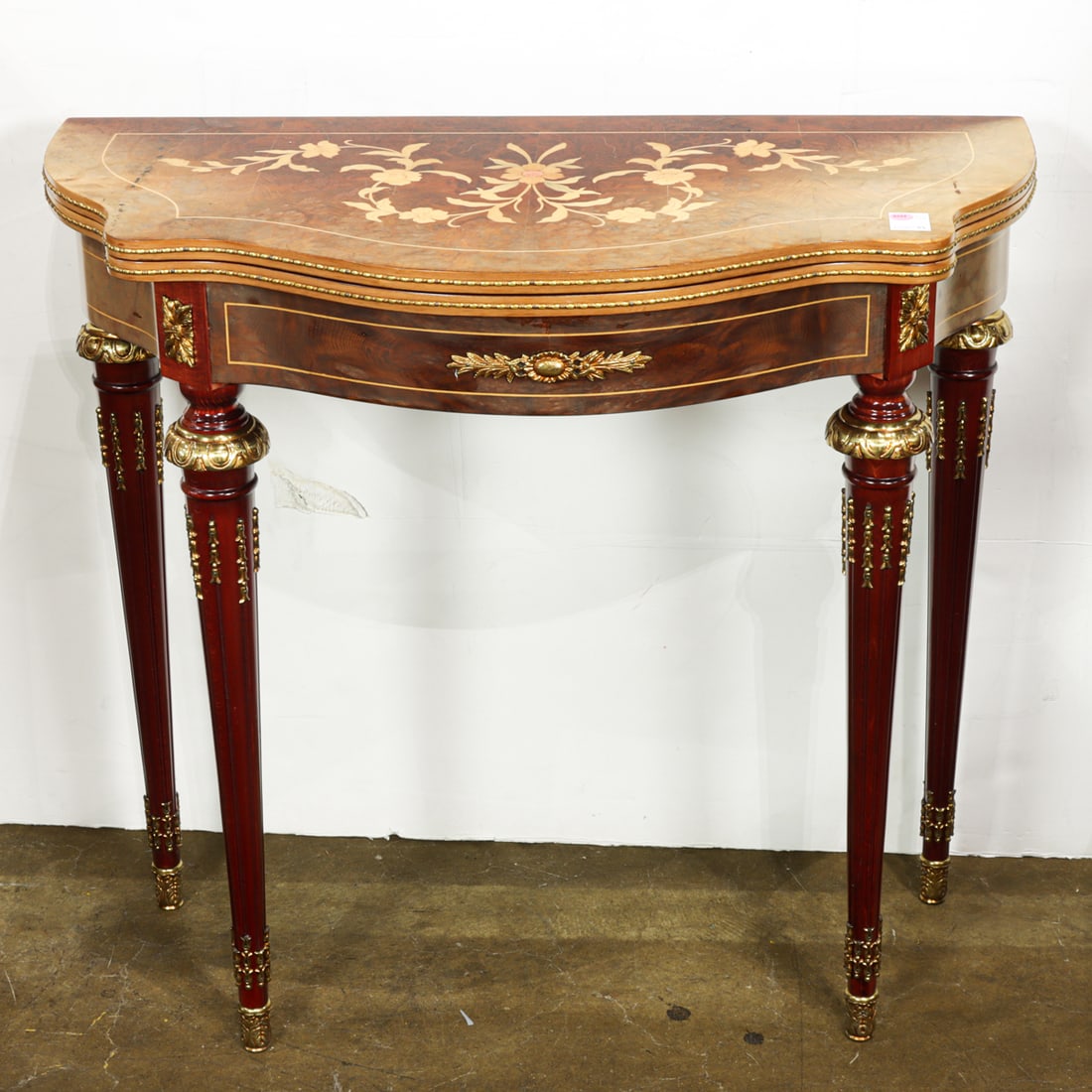 An inlaid flip top games table with a serpentine apron: An inlaid flip top games table with a serpentine apron, opening to a felt lined playing surface, and resting on tapered legs, 32"h x 34.5"w x 17"d; open 32"h x 34.5"w x 34.5"d