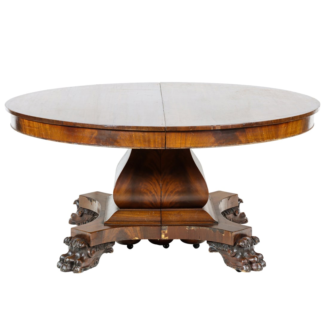 An Empire Revival dining table: An Empire Revival dining table, circa 1900, the circular top above the large pedestal base raised on paw feet, together with two original leaves with aprons, 29.5"h x 60"w (closed)