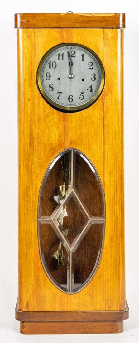 An Art Deco wall clock: An Art Deco wall clock, circa 1940, with bevel glass door, brass dial, weights, and pendulum, 33.5"h x 11"w
